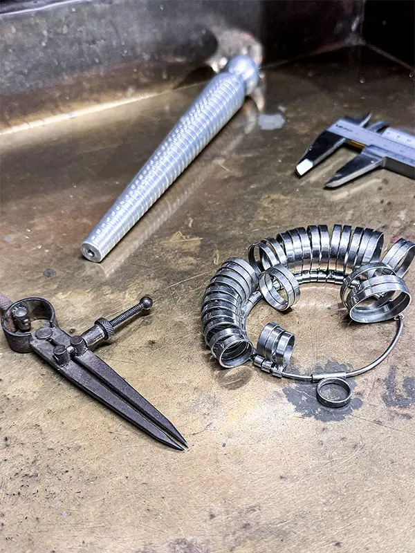 O resultado final é apenas uma parte de algo maior. O trabalho não está no objeto acabado, mas no caminho que o constrói: as escolhas que traçam o percurso, o diálogo com o material — que possui sua própria voz — e o ato de criar, que é também um ato de descobrir. Não se trata apenas de fazer por fazer; cada peça precisa ter um porquê. Sem isso, seria apenas mais uma entre tantas no mundo. Meu processo começa antes de chegar à bancada. Ele nasce de projetos que surgem do meu repertório de vida, feitos de perguntas, pesquisas e reflexões. Pensamentos viram palavras, que apontam caminhos para as ideias fluírem, como um diálogo entre intenção e descoberta. Essas palavras não delimitam, mas apontam direções. Meu trabalho toma forma como uma escultura que emerge entre o controle e o acaso. Não sigo um plano rígido; cada escolha que faço carrega vestígios de tudo o que já experimentei e a promessa do que ainda posso criar. É nesse encontro entre material e gesto que algo se revela, pensado, mas sempre aberto ao inesperado. O tempo guia meu trabalho. Não o tempo que os relógios contam, mas um tempo que avança e retorna, que se dobra e se perde, como um sonho que não consigo lembrar. Esse tempo não é linear; é um labirinto, que vive no presente, guarda ecos do passado e abre portas para o futuro. Na joalheria, o valor dos materiais é, muitas vezes, definido por seu preço: ouro é joia; bronze, não. Mas, para mim, joia é o que o joalheiro cria. Independe de sua raridade ou brilho. A joalheria em que acredito não se prende a hierarquias, mas explora possibilidades. Cada material traz algo único e amplia o sentido do trabalho. Minhas peças nascem desse intervalo entre o que procuro e o que encontro, essa busca incessante por respostas que talvez nunca se revelem por completo. É nesse espaço que encontro o belo — não o que se vê, mas o que se sente, nas camadas de cada peça. Entre o que desaparece e o que persiste está o sentido do que faço — como humana, como criadora, como alguém que busca algo, de um tempo que só existe no instante em que é criado.